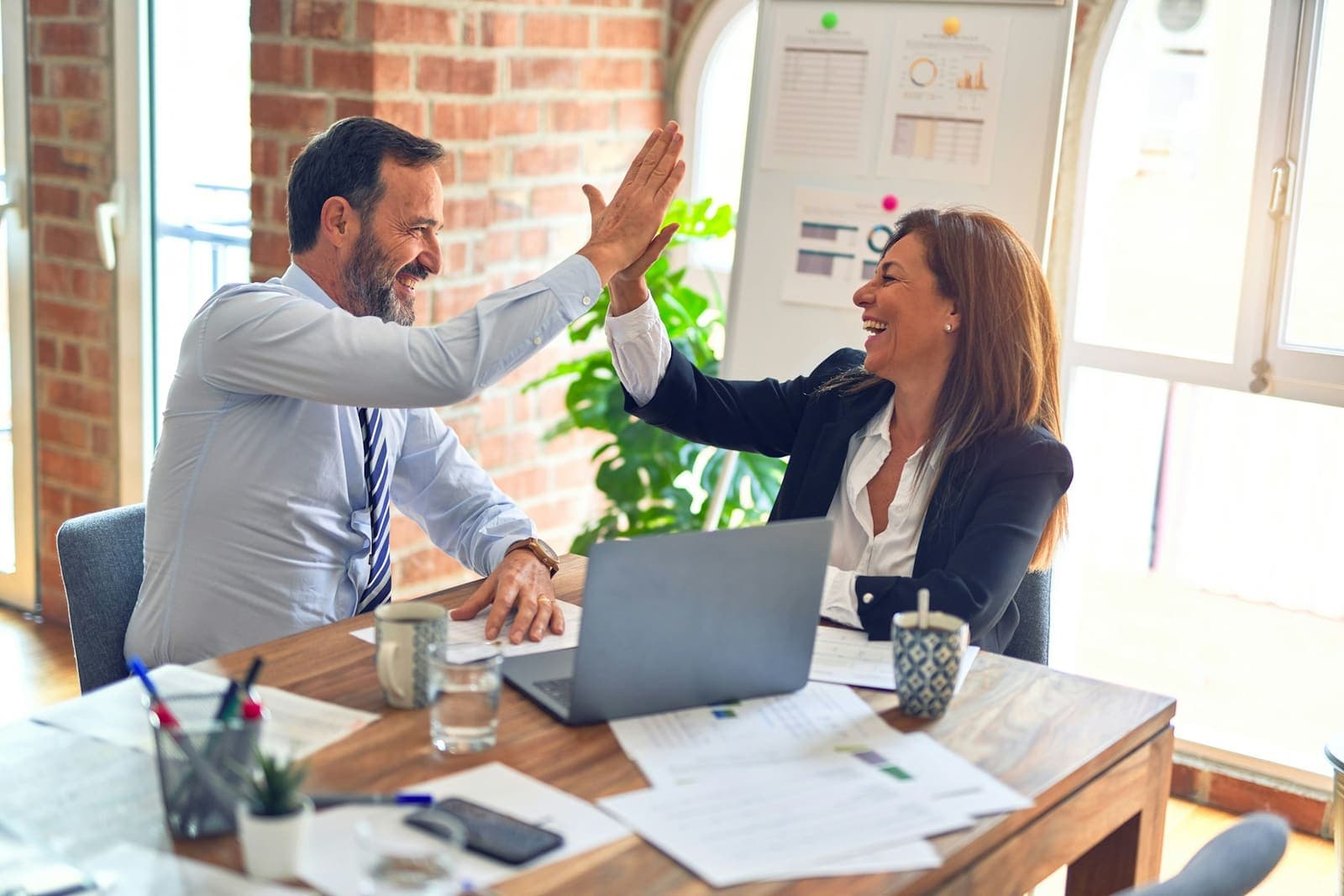 Two colleagues celebrating successful business results at their desk