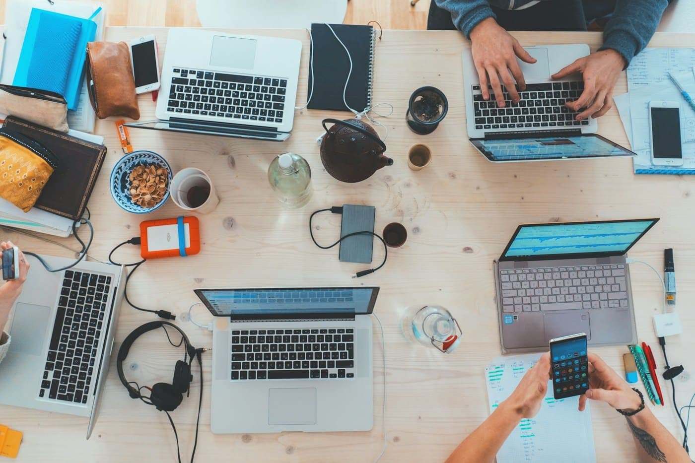Top view of a team working together at a shared desk with laptops and notebooks